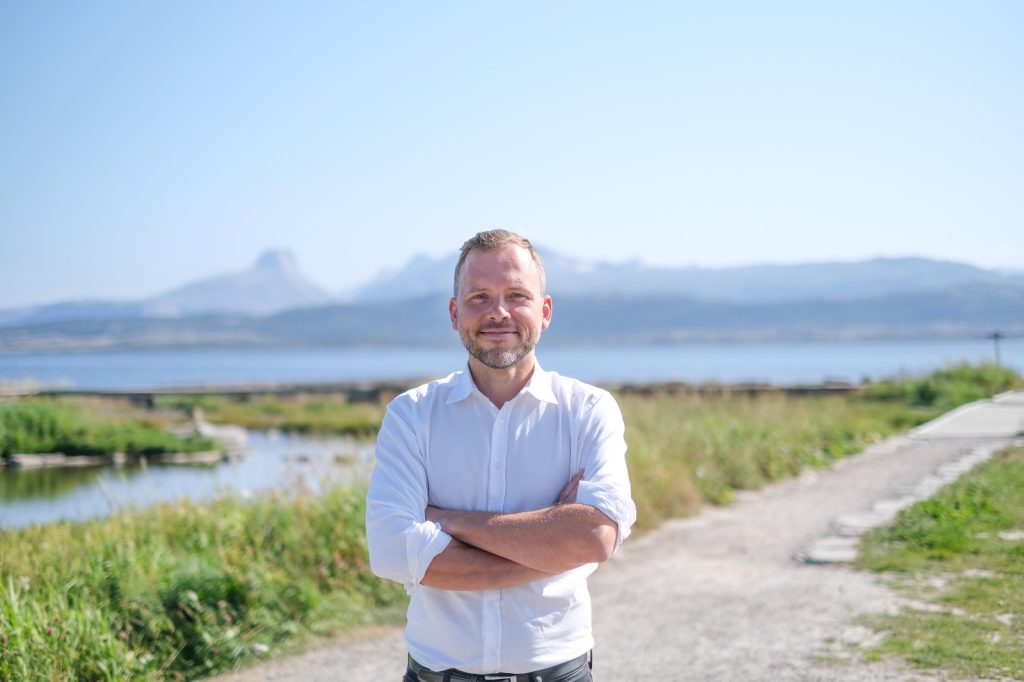 Bilde av Audun Lysbakken med utsikt til fjell og hav i bakgrunnen. 